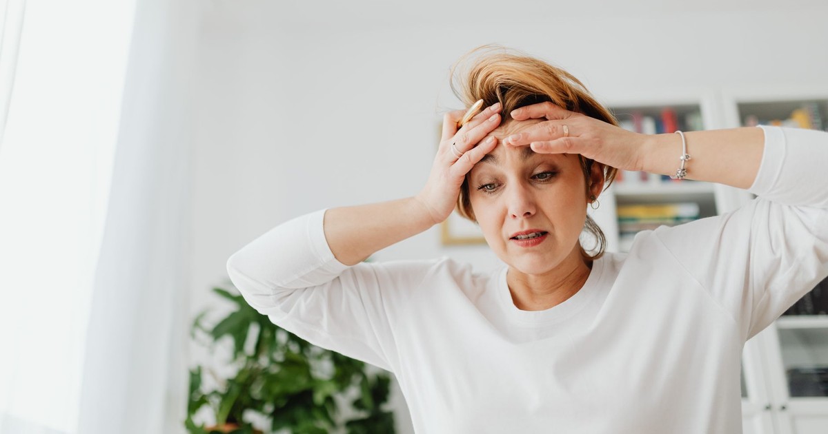 A worried woman indoors with hands on forehead, expressing stress.