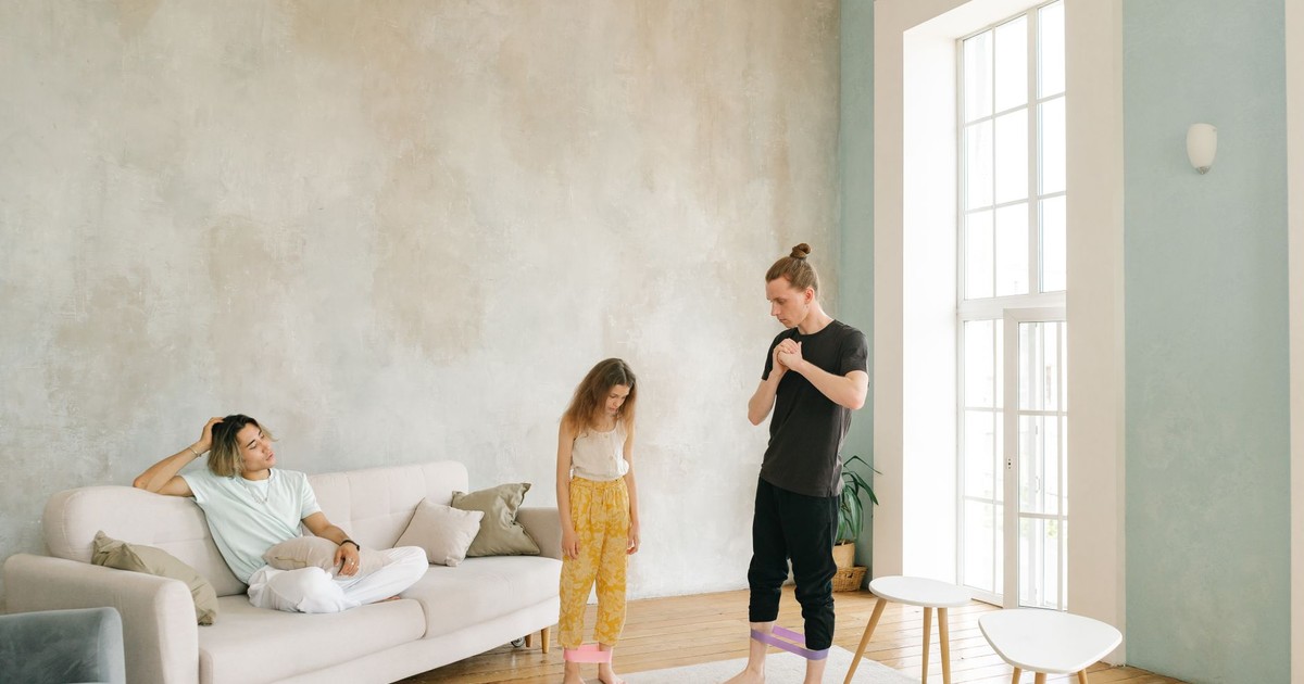 A family exercises indoors using resistance bands in a bright living room.