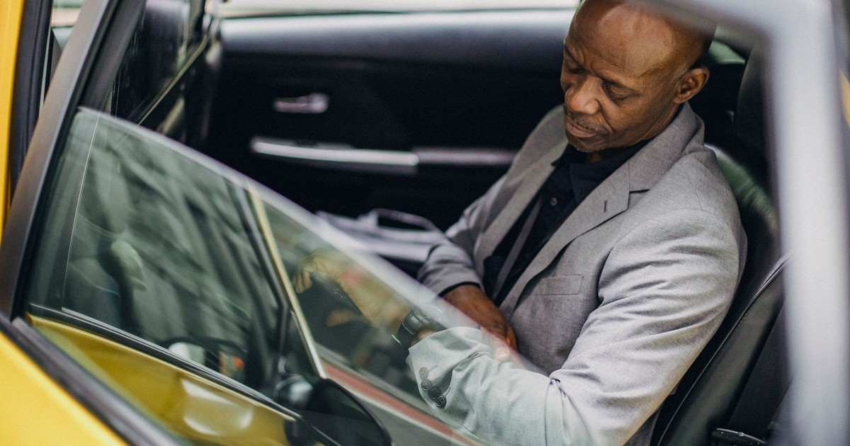 Side view punctual adult African American businessman in formal clothing sitting in taxi car and checking time on wristwatch