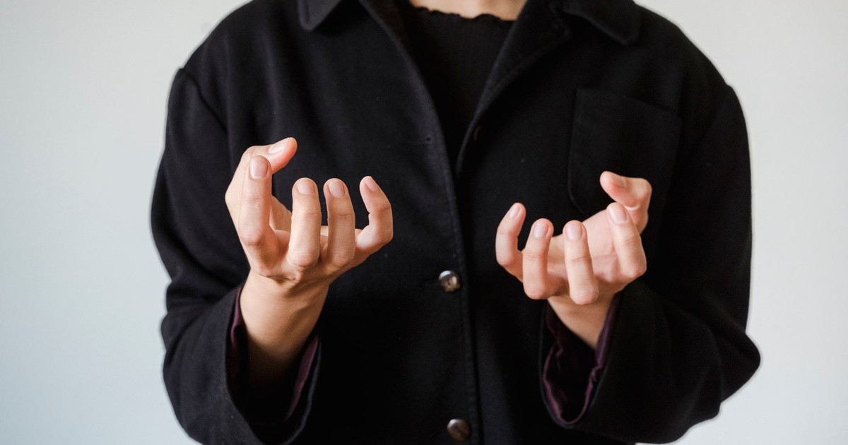 Close-up of person in black coat making expressive hand gesture, highlighting emotion.