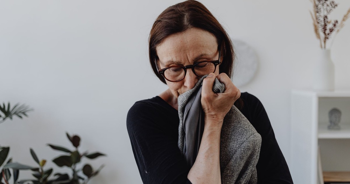 A middle-aged woman grieves while holding a cloth in an indoor setting.