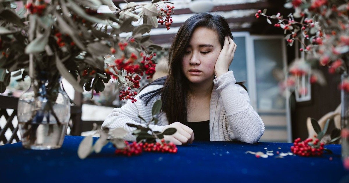 A thoughtful woman sitting at a table with red berries and greenery.