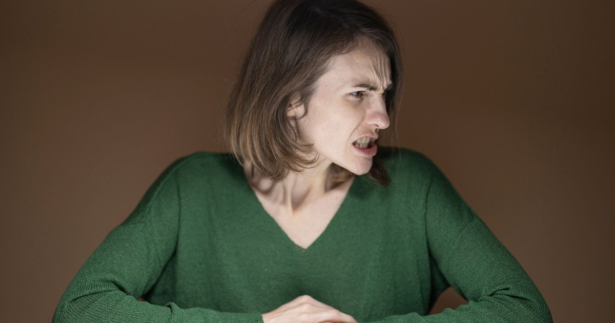 Portrait of an angry woman in a green sweater sitting indoors, looking sideways.