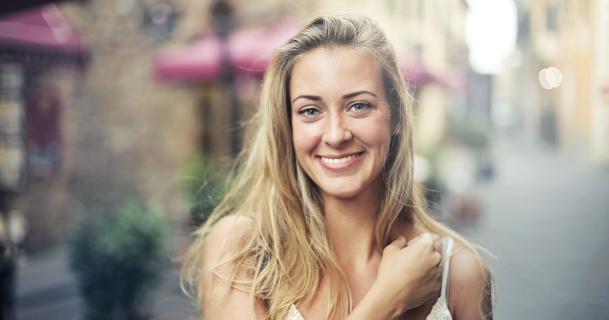 A happy woman with long hair poses on a sunny street, exuding joy and casual elegance.