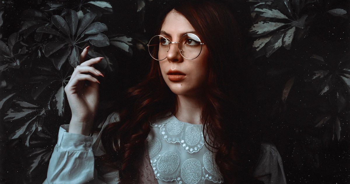 Portrait of a woman with eyeglasses in a vintage lace blouse surrounded by foliage.