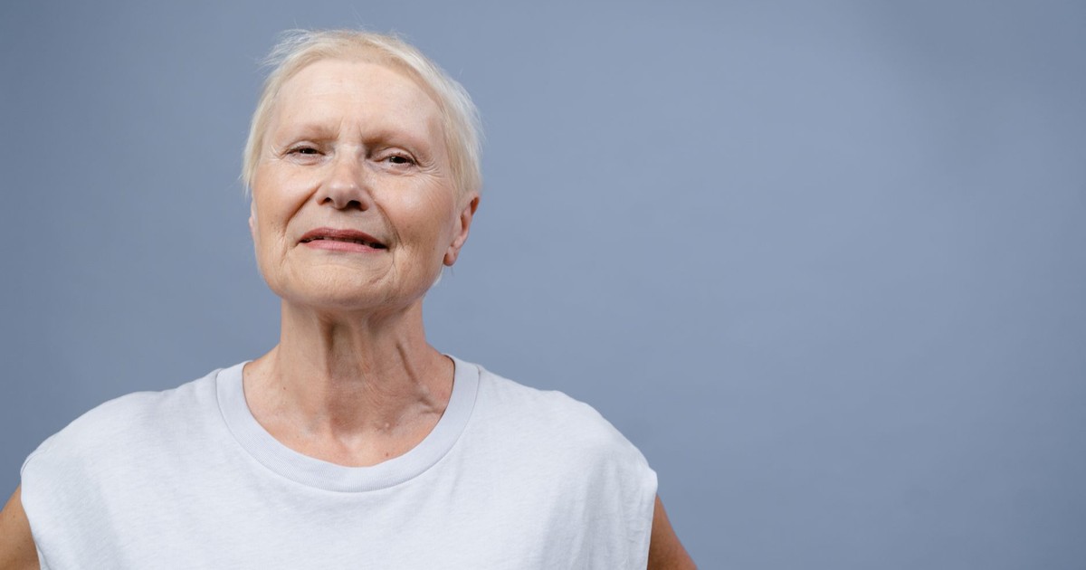 Senior woman with a gentle smile in a minimalist studio portrait, evoking warmth and positivity.