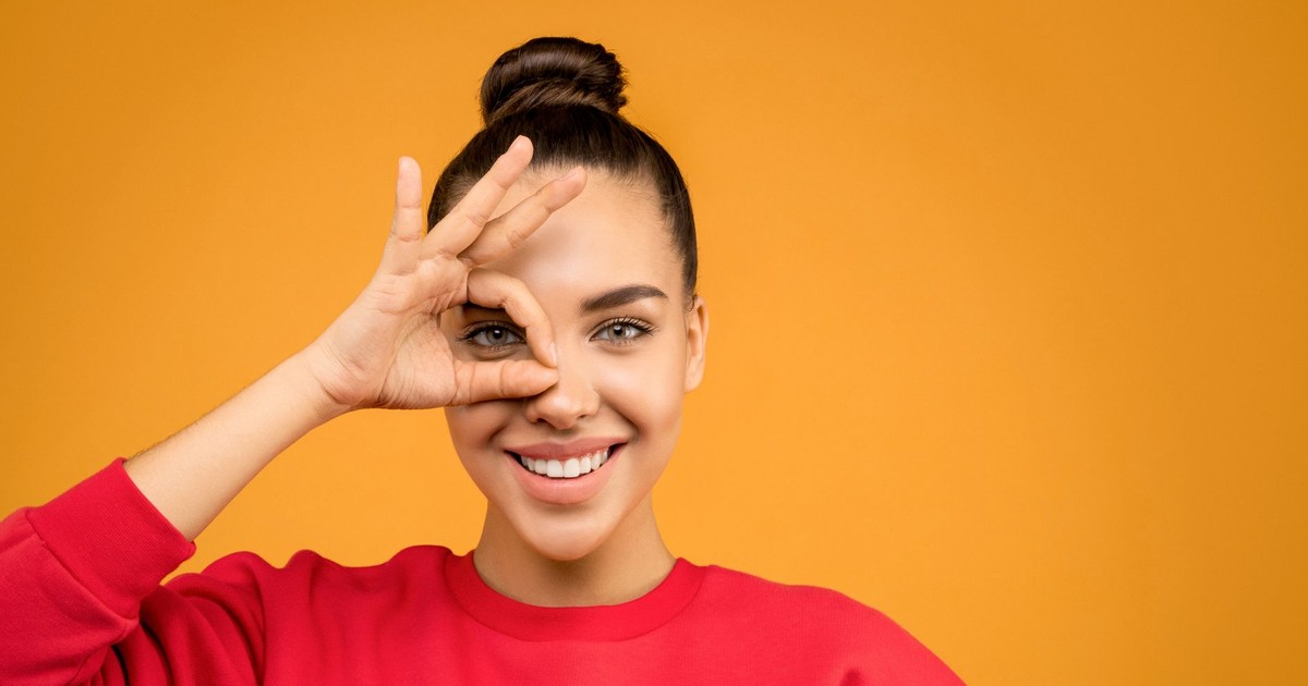 Smiling woman making a playful hand gesture against a vibrant orange background.