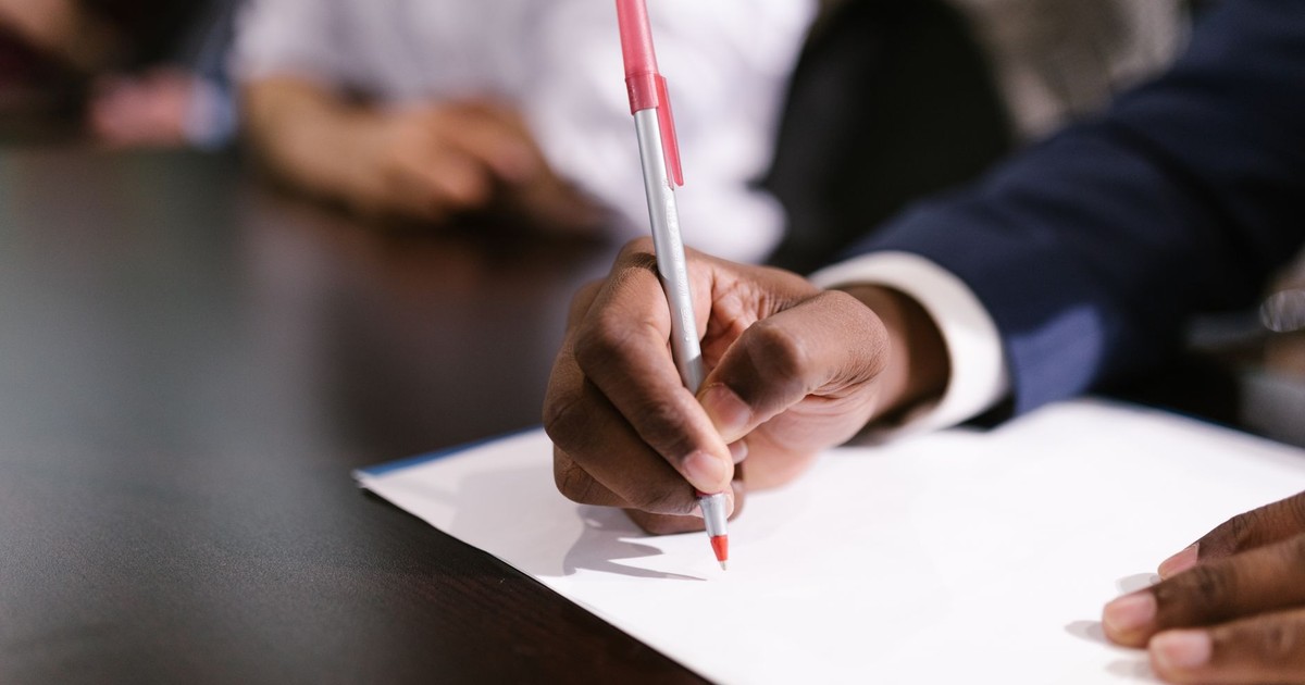 An individual writing on white paper in a professional setting, focusing on the hand and pen.