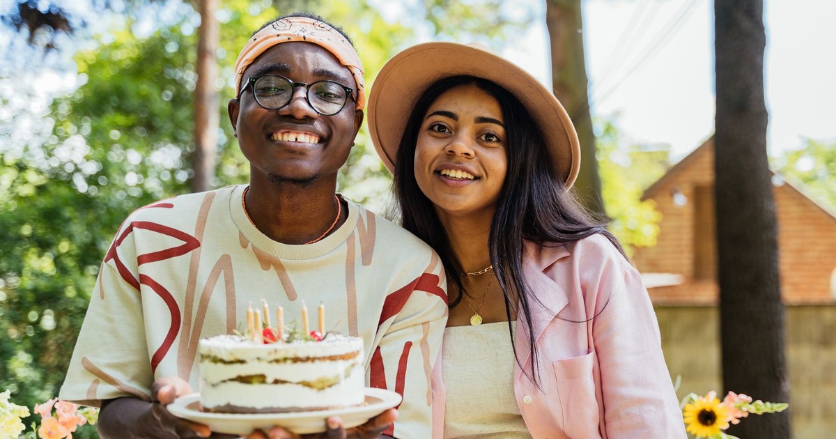 Two adults celebrating a birthday outdoors with a cake adorned with candles, smiling and happy.
