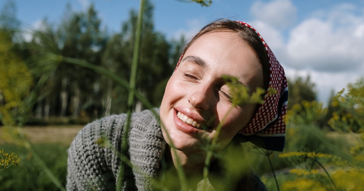 A joyful woman in a headscarf enjoying a sunny day outdoors, surrounded by greenery.