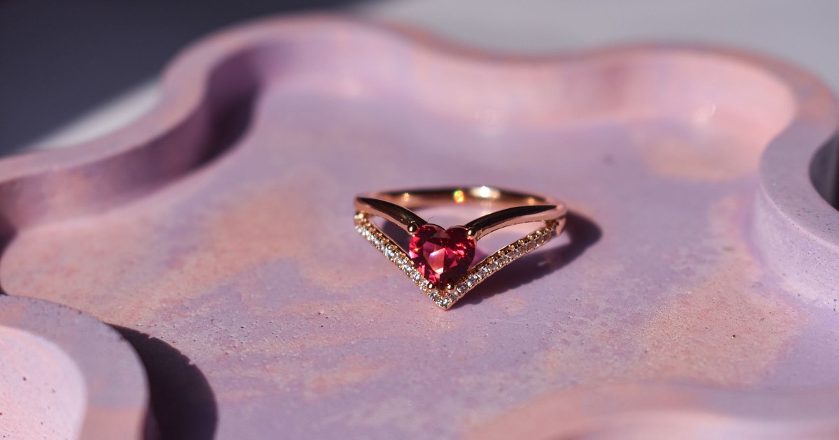 Close-up of a heart-shaped gemstone ring on a pink decorative tray.