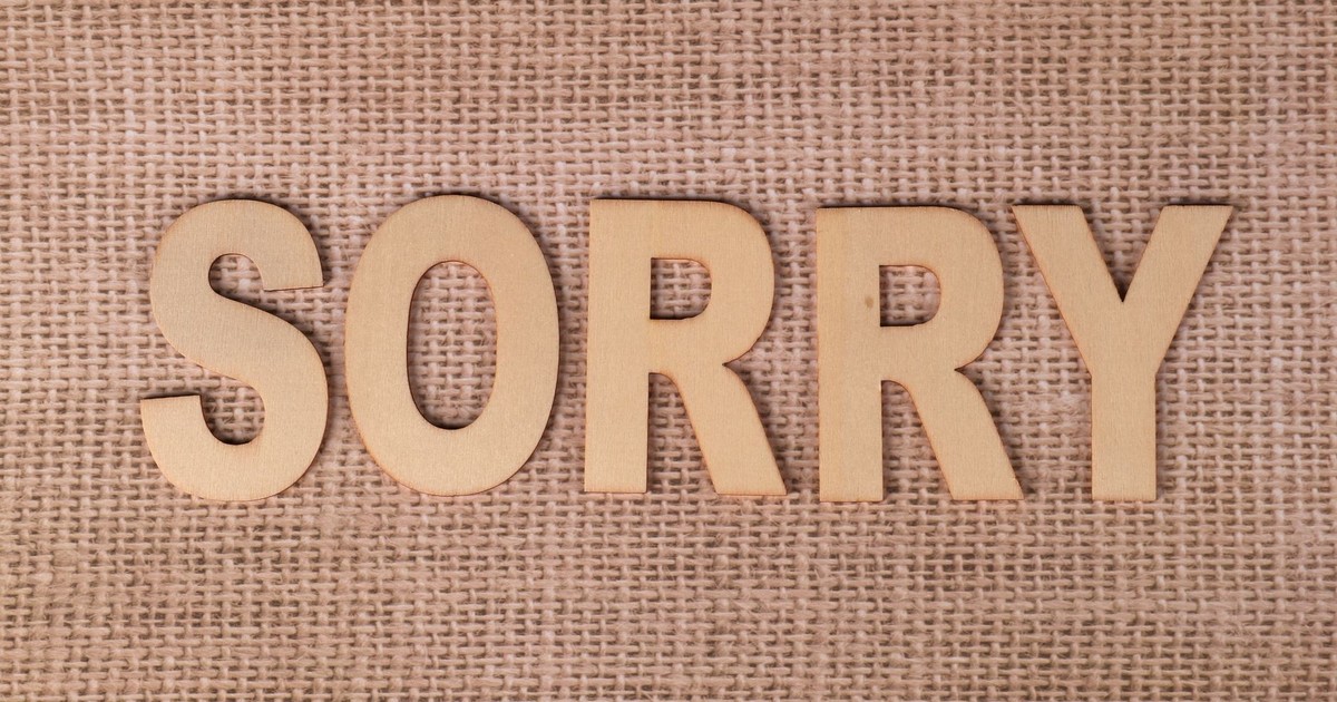 Wooden letters forming the word 'sorry' on a burlap fabric background.