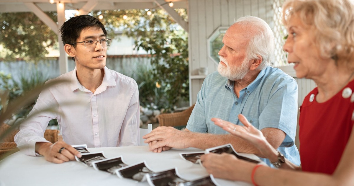Senior couple and family member discussing ultrasound photos at an outdoor table.