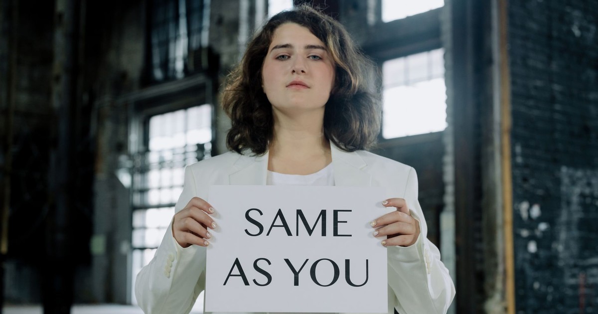 Person holding a 'same as you' sign in an industrial space, symbolizing equality.