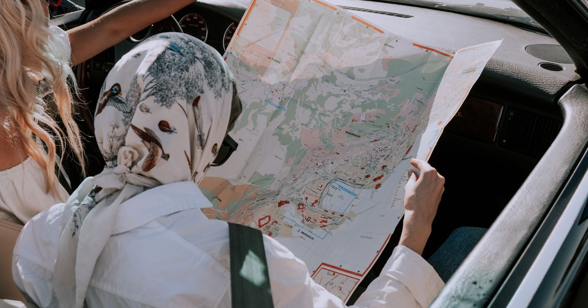 Two friends in a car navigating their road trip using a map during daytime.