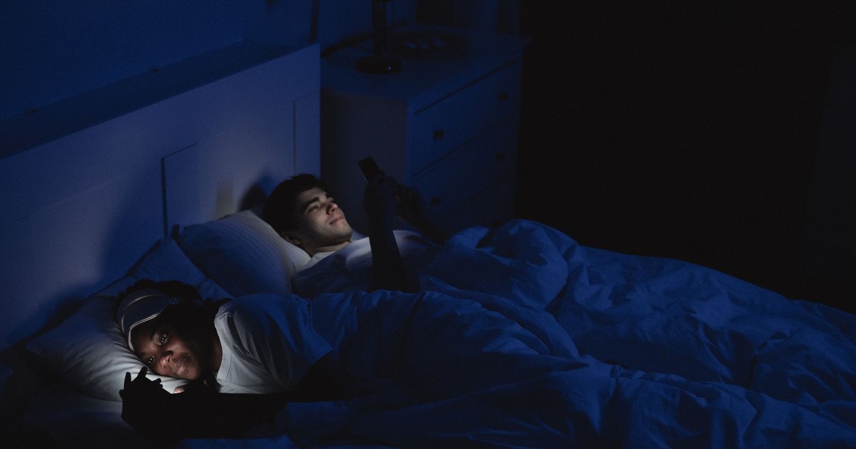 Couple lying in bed at night using gadgets, low light and relaxed mood.