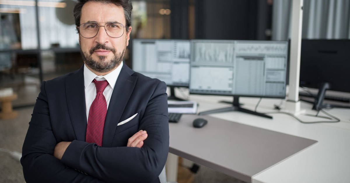 Business professional in corporate attire with arms crossed in a modern office space.
