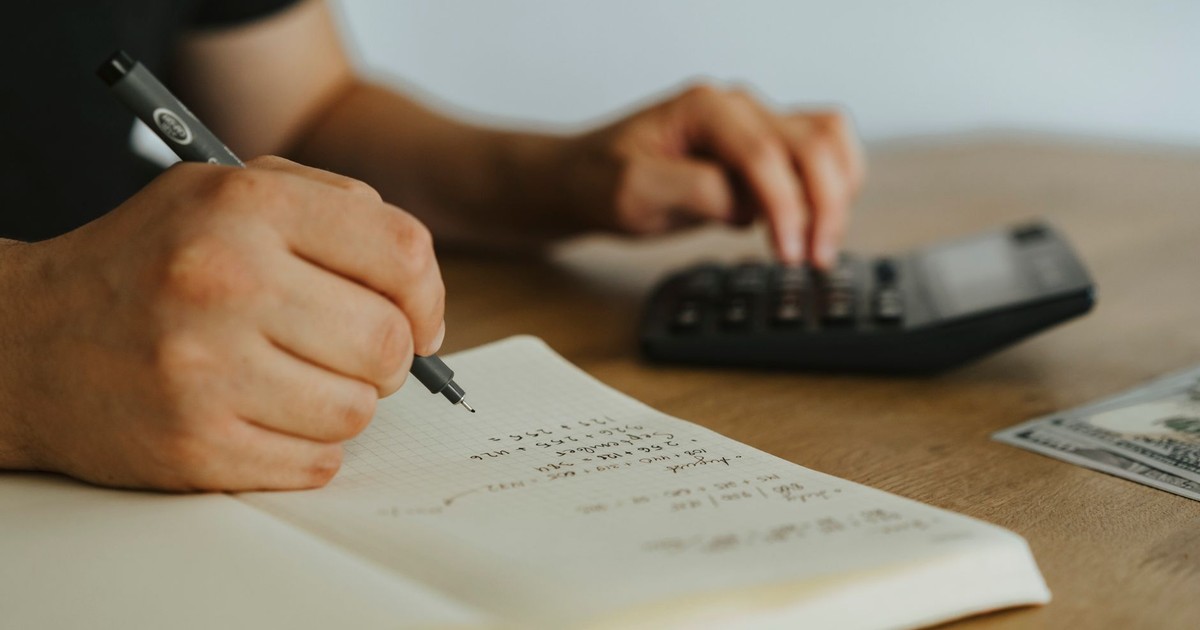 Close-up of hands writing calculations in a notebook with a calculator, focused on budgeting or financial work.