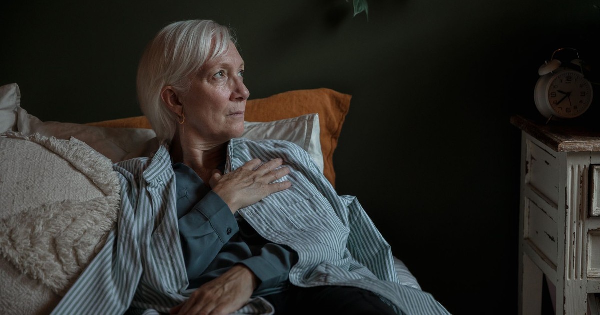 A senior woman with white hair looks contemplative while reclining at home, conveying introspection and calm.