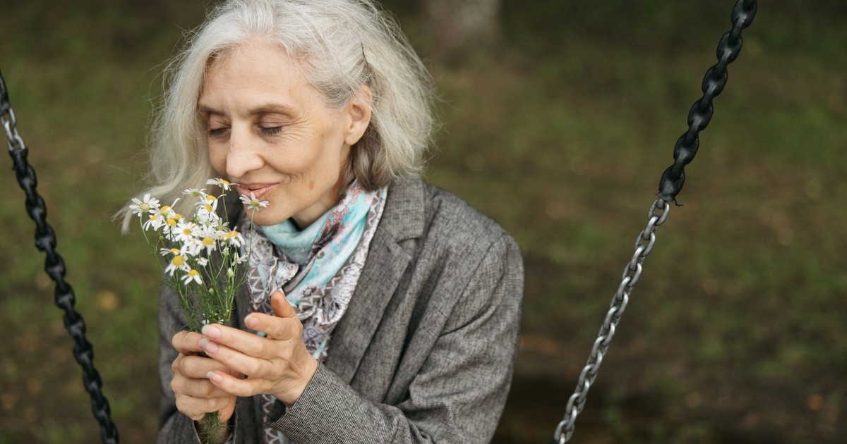 Elderly woman savoring the scent of wildflowers while seated outdoors.