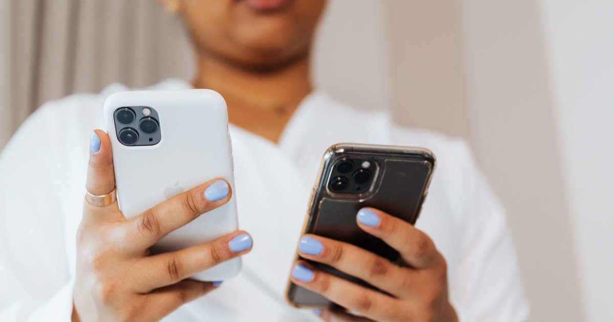 Close-up of a person with blue nails holding two smartphones indoors.