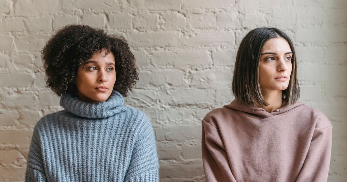 Sad African American woman with female friend in casual clothes looking away while sitting in light room during quarrel at home