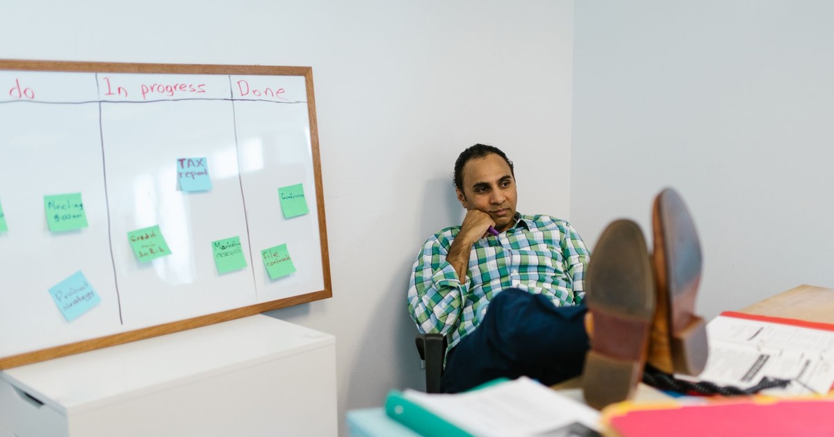 Man in casual attire relaxing at his office desk, contemplating work on a kanban board.