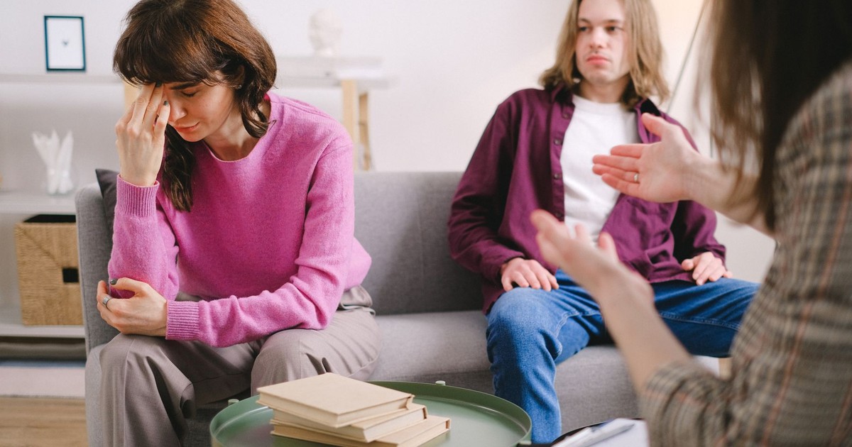 A couple undergoing therapy, expressing emotions on a sofa in a counseling office.