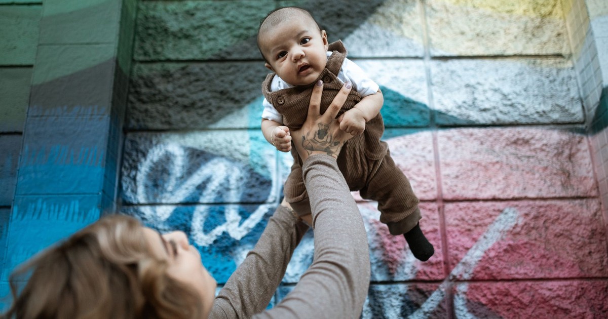 Joyful moment of a baby being lifted by a parent against a colorful graffiti wall.