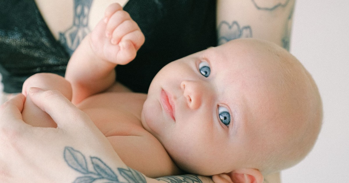 A beautiful baby with blue eyes held gently by tattooed arms, showcasing love and innocence.