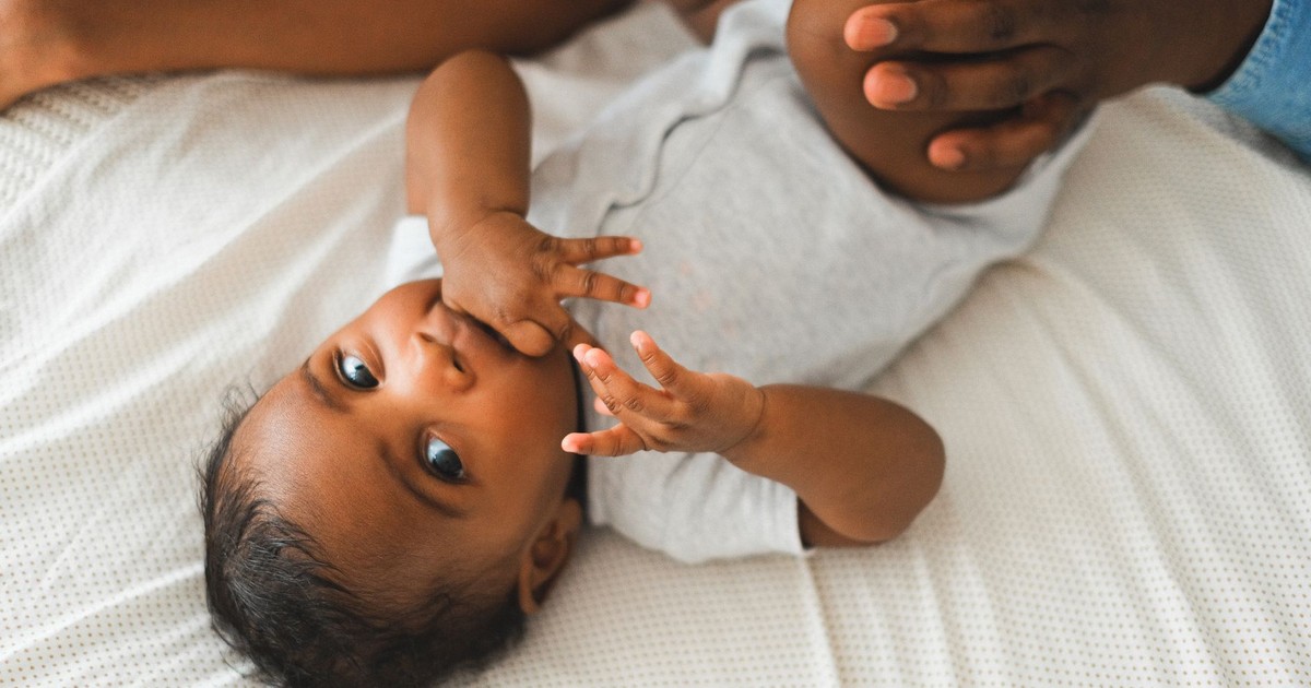 Cute baby in a onesie lying on a bed with parent's hands nearby, creating a warm and loving atmosphere.