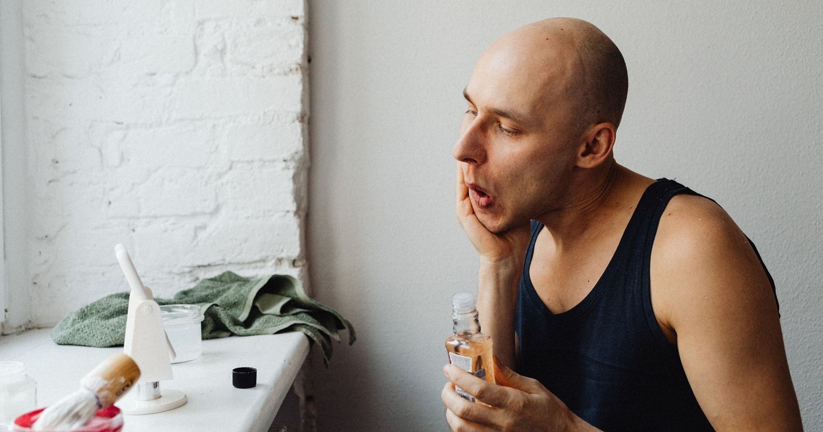 Adult man applying aftershave lotion in a bright bathroom, focusing on skincare routine.