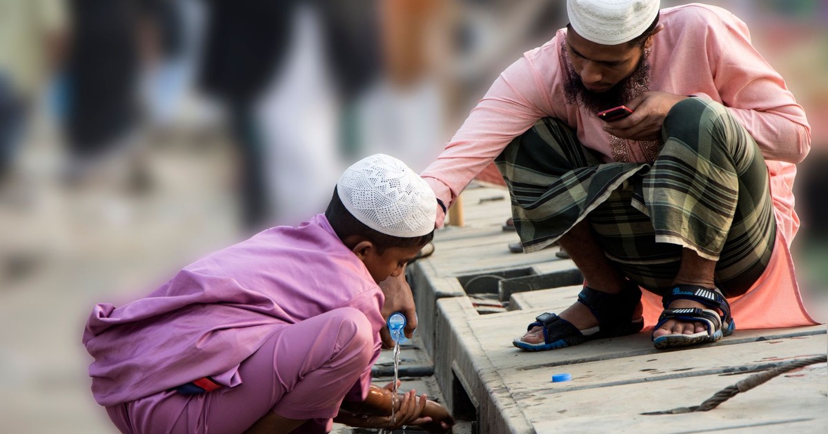 A father and son share a moment beside a small stream, both wearing traditional attire.