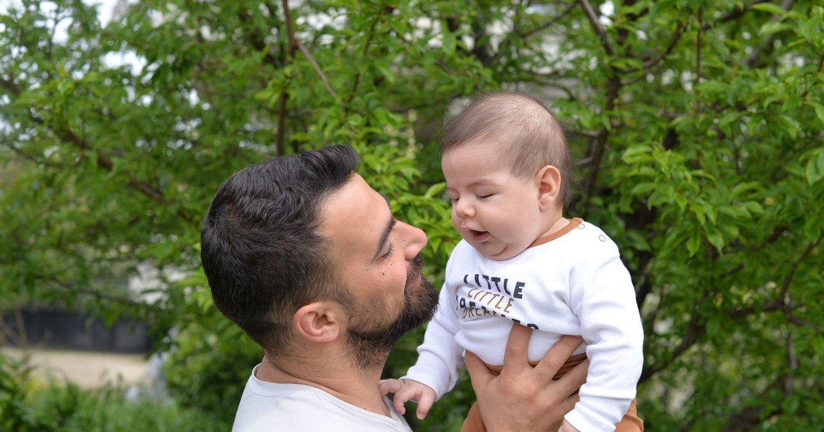A loving father holds his baby son outdoors amidst lush greenery, showcasing fatherhood and care.