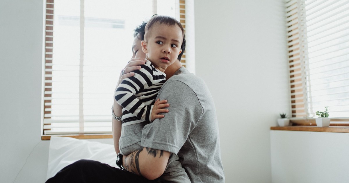 Father holding and comforting his young son by the window, showcasing warmth and family bond.