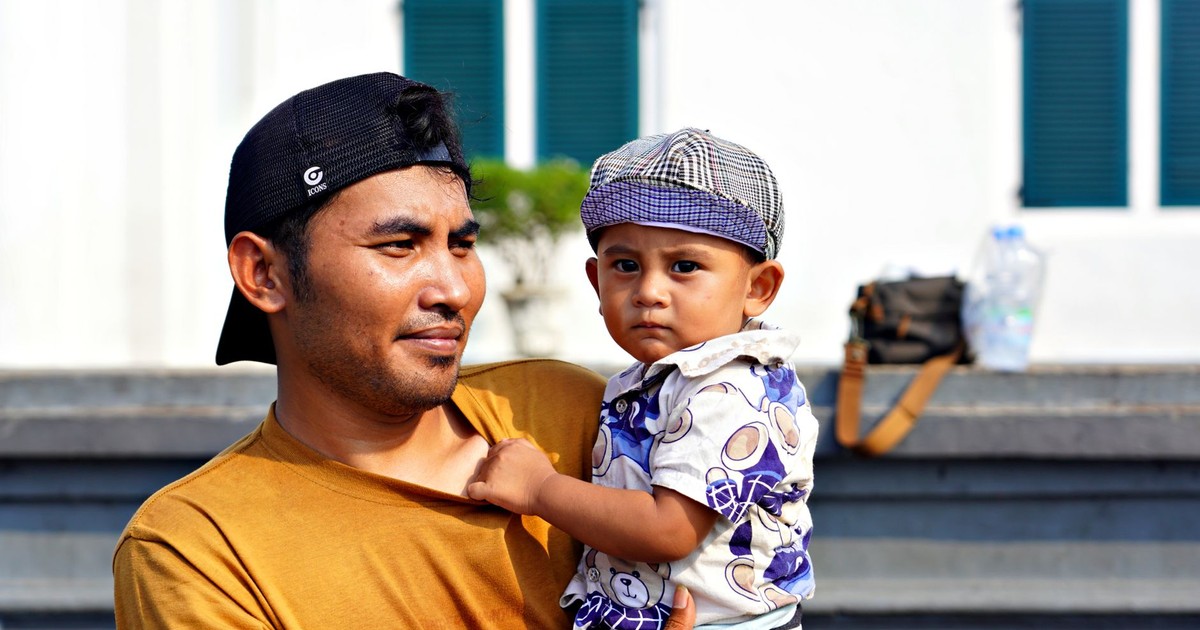 A father holds his young son while enjoying a sunny day outdoors.