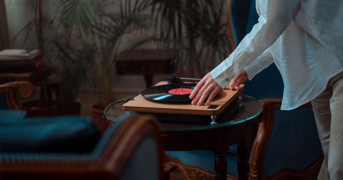 A person adjusting a vinyl record on a turntable in a cozy indoor setting.