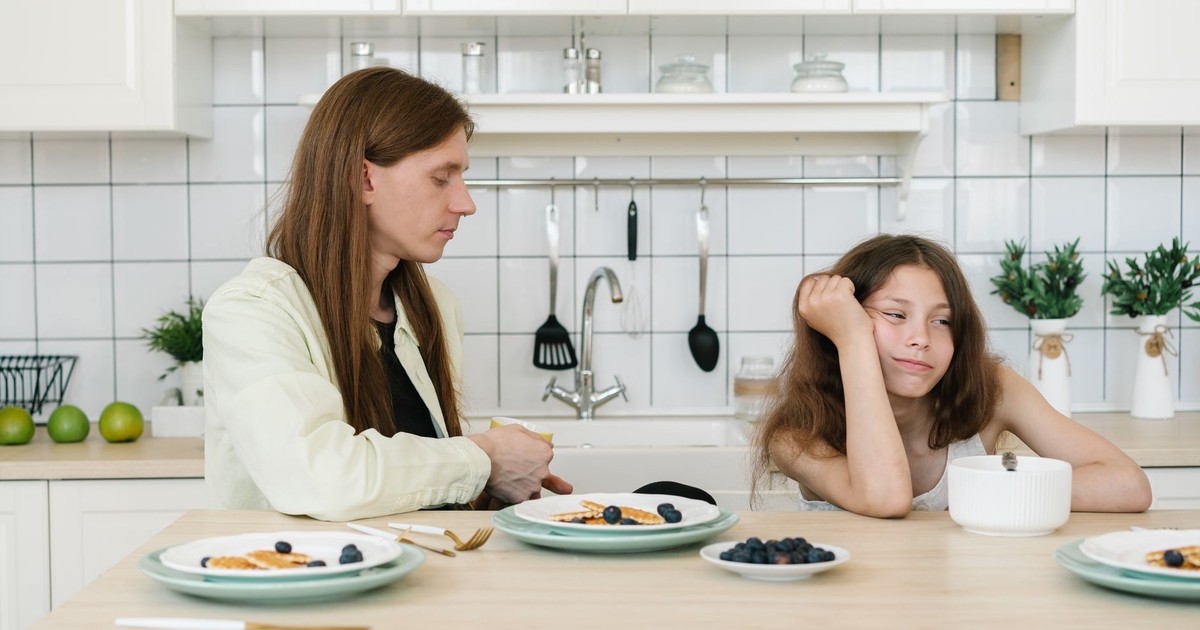 A man and girl sitting at a kitchen table with breakfast bowls and plates on a calm morning.
