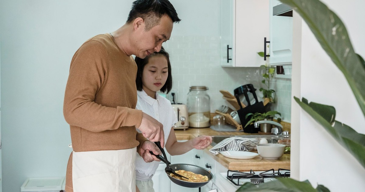 A father and his daughter cooking scrambled eggs together in their kitchen.