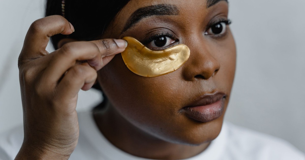 Close-up of a woman applying gold eye patches for skincare routine.