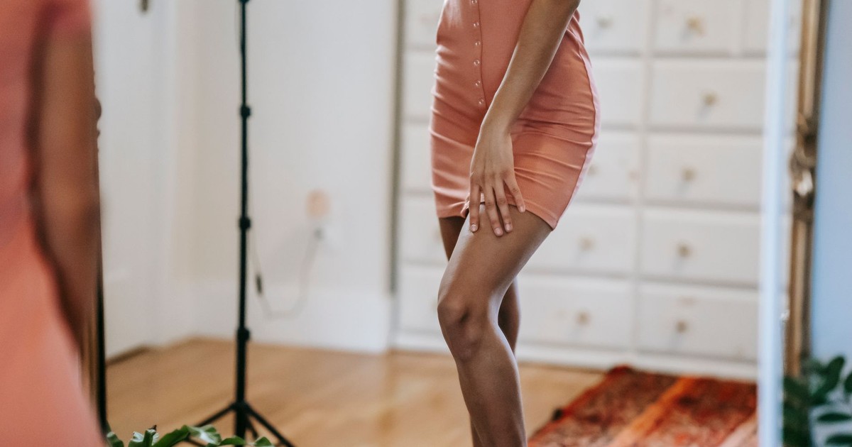 Crop unrecognizable female in dress touching thigh while reflecting in mirror in house room