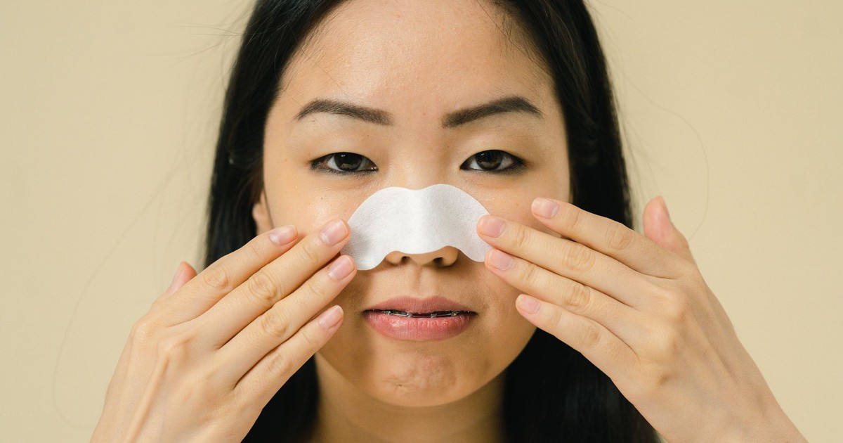 Close-up portrait of a woman using a nose strip for skin care treatment in a studio setting.