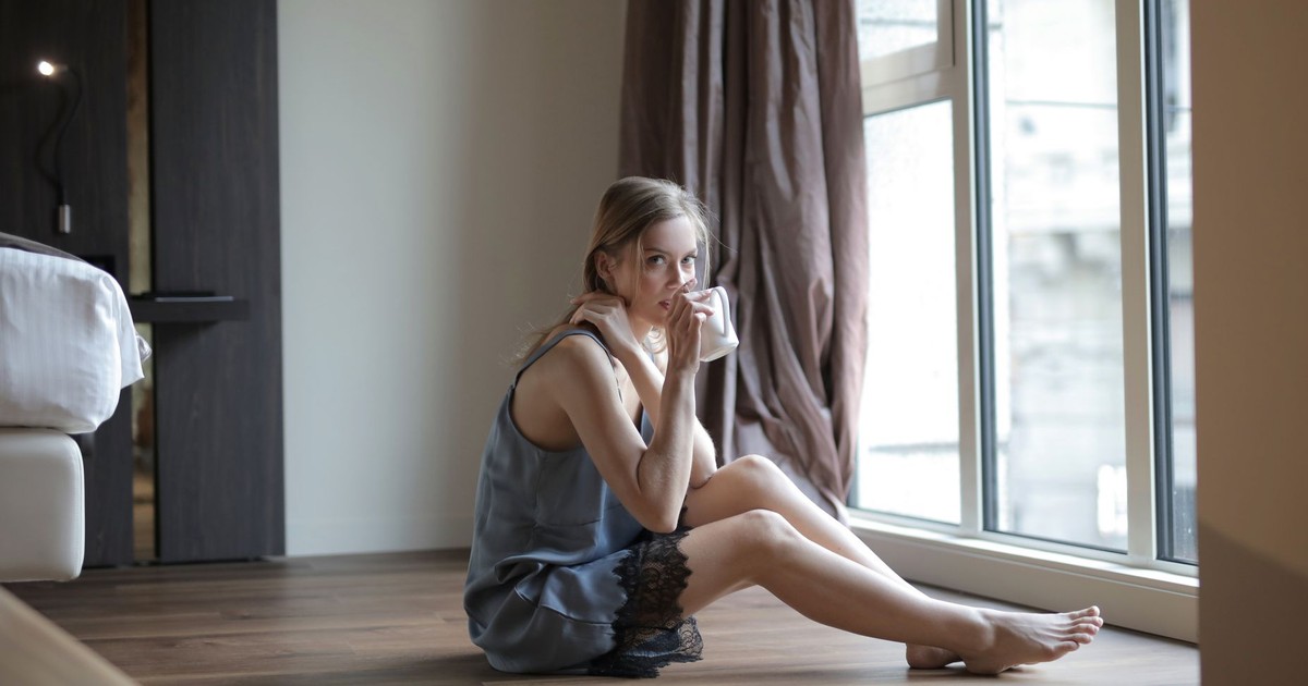 Relaxing scene of a woman sipping coffee by a window in a cozy home setting.