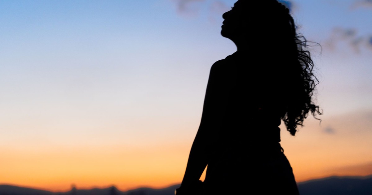 Silhouette of a woman with curly hair gazing at a vibrant Mexico City sunset.