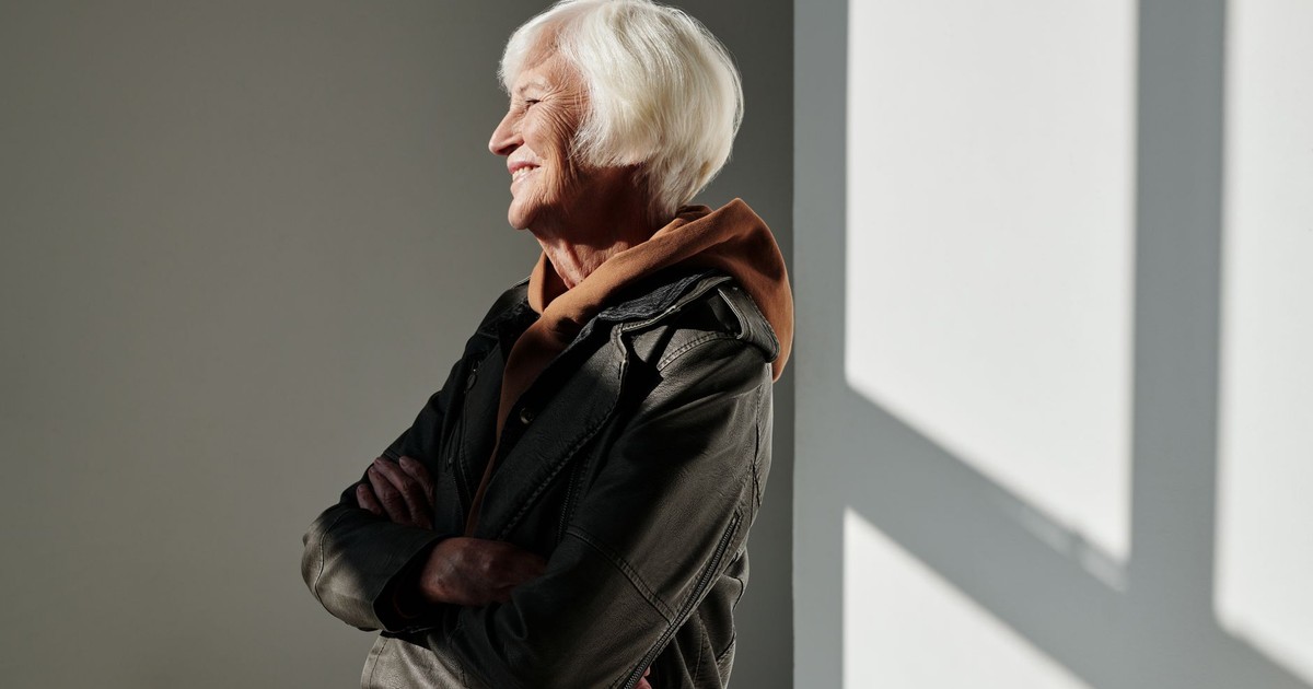 Senior woman in black leather jacket smiling confidently indoors, embracing stylish fashion.