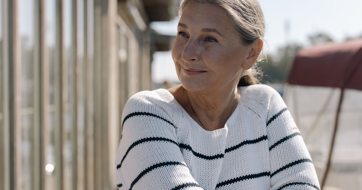 Charming portrait of a senior woman relaxing outdoors, wearing a cozy striped sweater and smiling warmly.