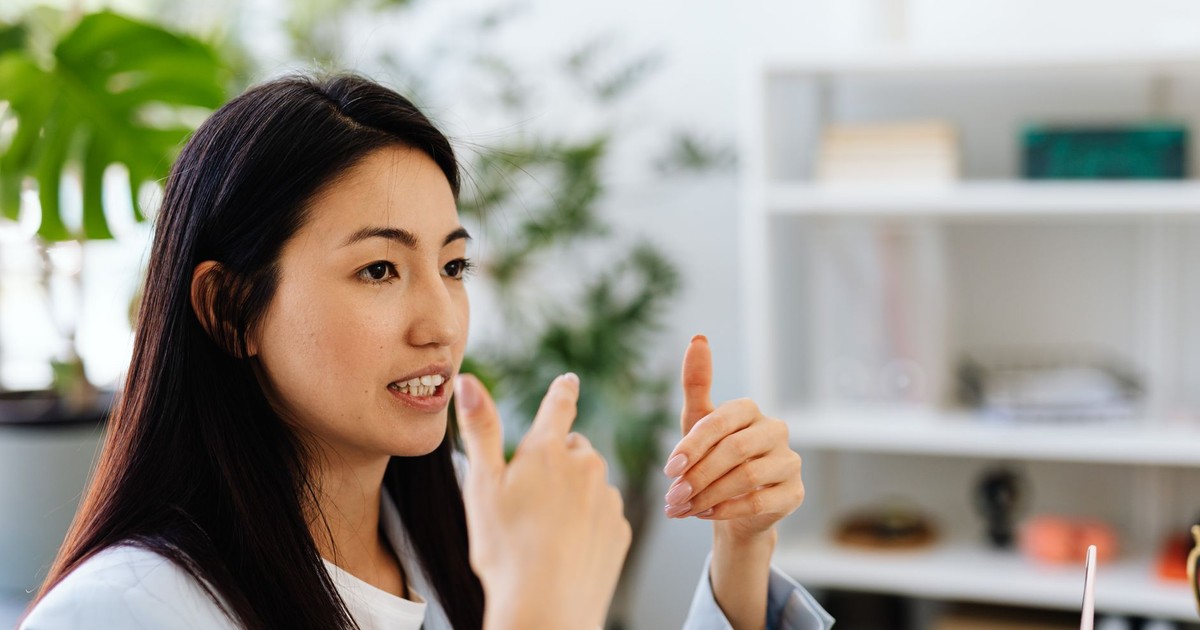 Asian woman gesturing in conversation in a modern office setting, showcasing communication.