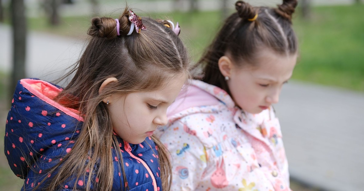Two young girls in winter jackets, contemplative in a park setting.