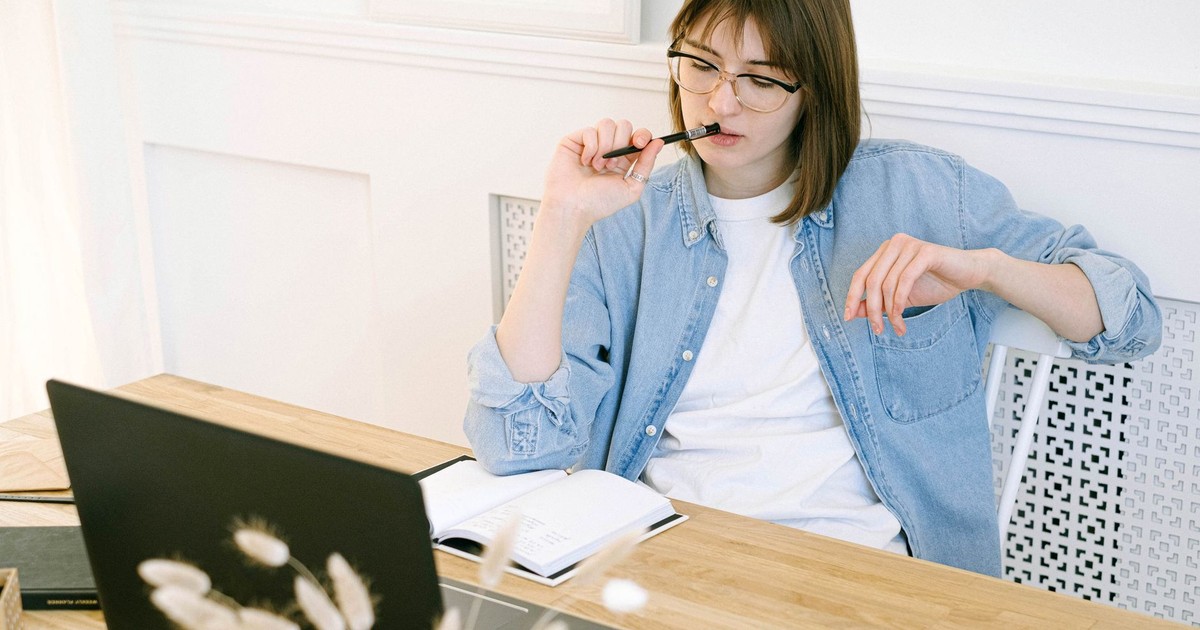 Woman working thoughtfully in home office, reflecting on ideas with laptop and notebook.