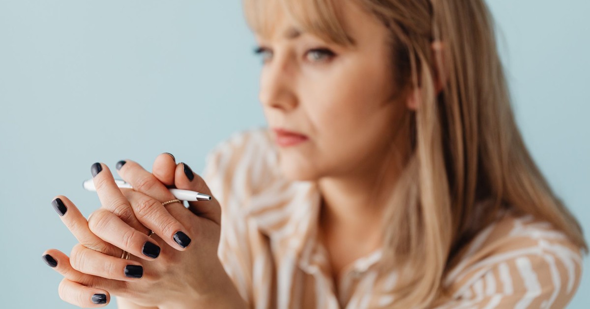 Blurred image of a woman holding a pen with a thoughtful expression, focusing on her hands.